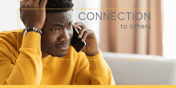 A distraught man in a yellow sweater talks on the phone, reaching out for support using connection to others as a technique for emotional regulation.