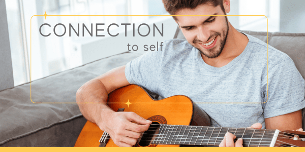 Happy man playing the guitar on his home on the couch, demonstrating connection to self by practicing authentic living exercises like incorporating play and fun into your life