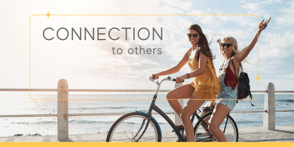 Two smiling women balancing on a bike, expressing authentic connection to others and play as a form of authentic living.